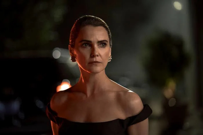 Person in an elegant off-the-shoulder dress looks seriously into the distance, set against a dimly lit background