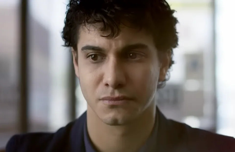 Walter O'Brien (Elyes Gabel) appears thoughtful, looking slightly downward. The background is soft-focused, suggesting an indoor setting
