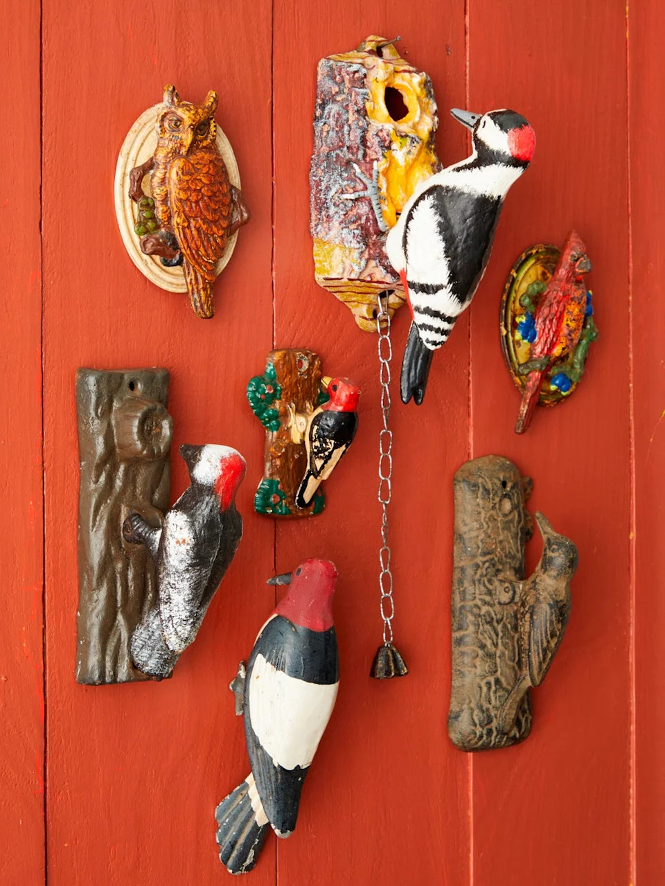 Colorful bird figurines mounted on a red wooden background, including owls and woodpeckers in various styles.