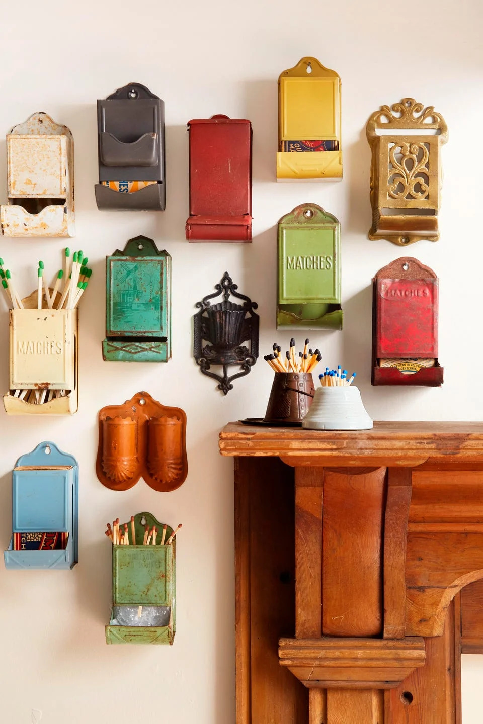 Wall display of assorted vintage match holders and decorative containers with matchsticks and utensils on a wooden shelf.
