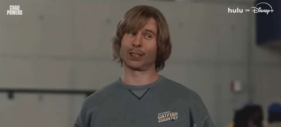 Man with long hair in a sweatshirt smiling while speaking in a casual setting