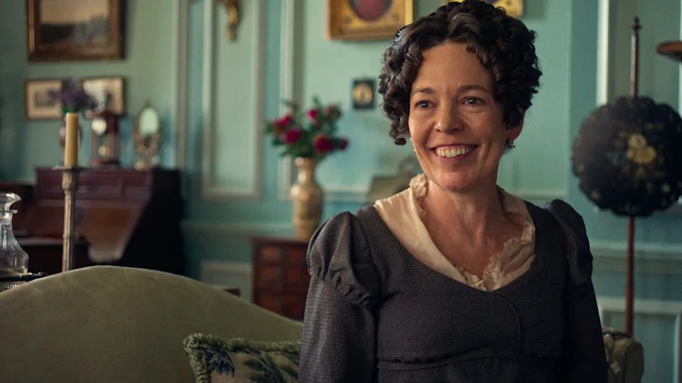 Woman with curly hair smiling in a vintage room with decorative furnishings and soft color palette.