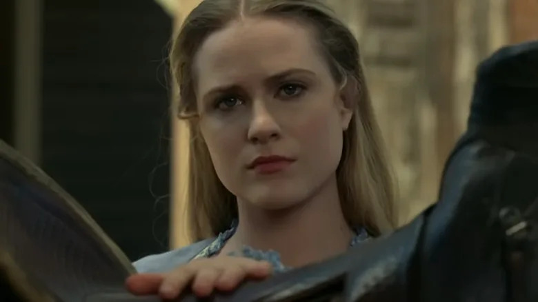 Dolores Abernathy looking over a horse's saddle out at someone in the park on Westworld