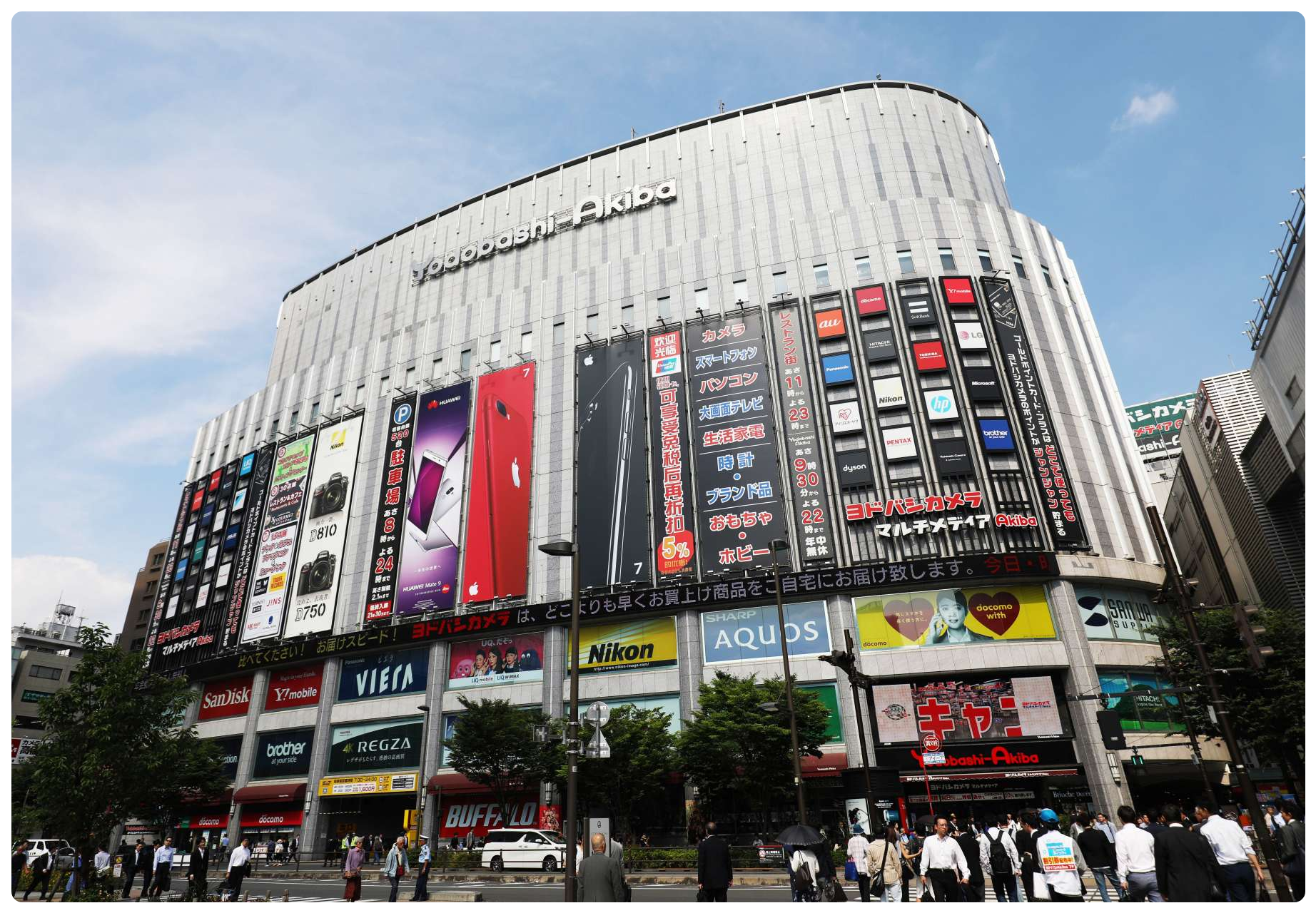 The Yodobashi Camera store in Akihabara, Tokyo, its multi-storey facade covered in large product advertisements above a busy street.