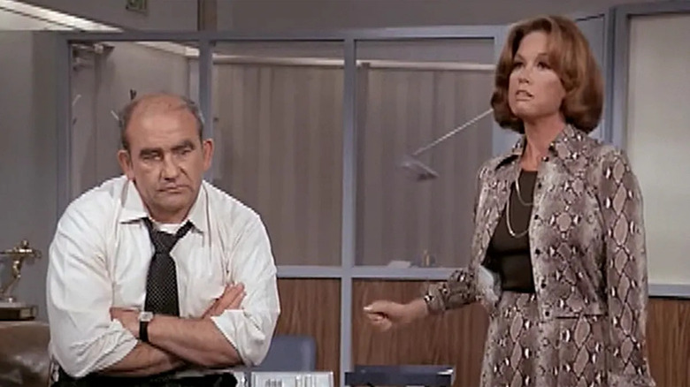 Ed Asner as Lou Grant folds his arms next to Mary Tyler Moore as Mary Richards on The Mary Tyler Moore Show