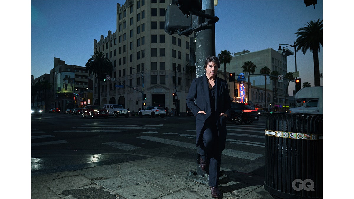 Tom Cruise stands in a dark suit at a street corner near Hollywood Boulevard.