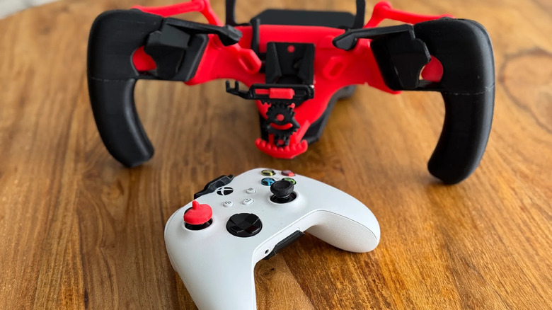 Xbox controller beside a red 3D-printed racing wheel attachment.