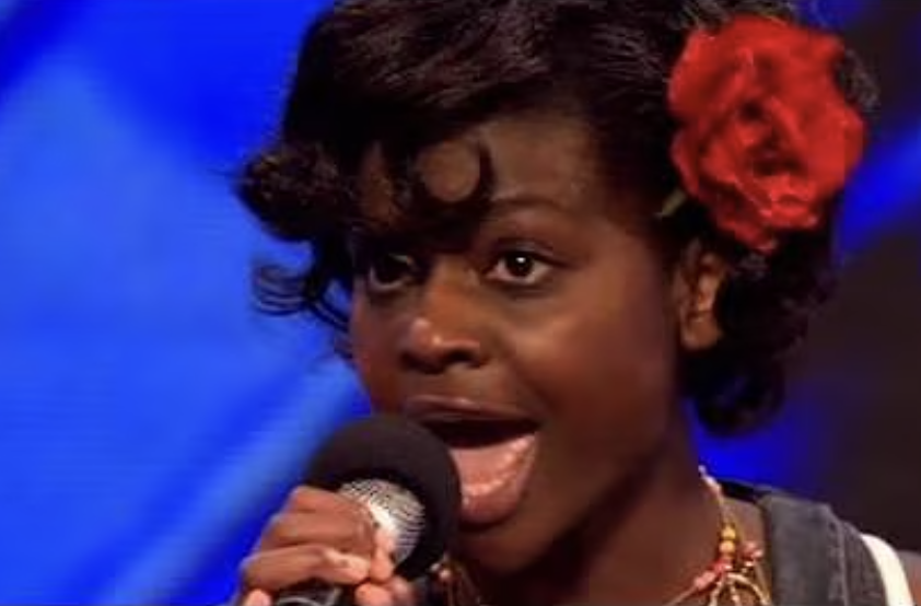 Person singing passionately into a microphone, wearing a flower in their hair, likely on a talent show stage