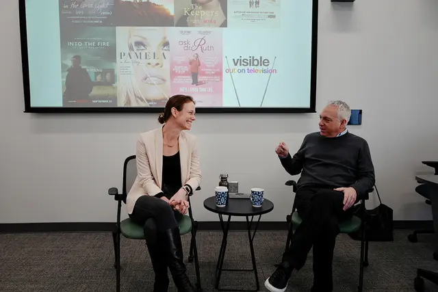 Two individuals talking in front of backdrop of documentary covers
