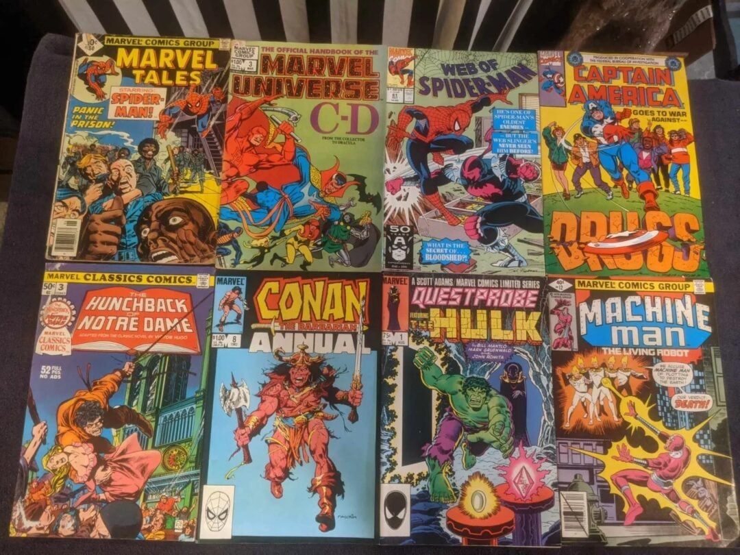 A collection of eight vintage comic books is displayed on a surface. The covers feature characters like Spider-Man, Hulk, Conan the Barbarian, and others in dynamic action poses with bold, colorful illustrations and text.