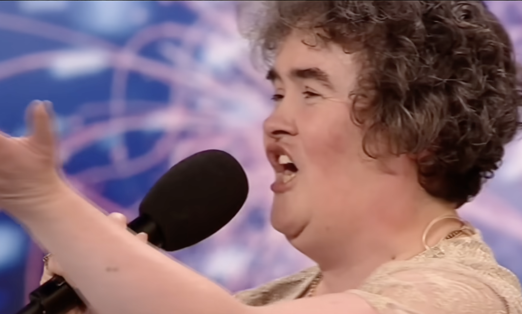 Person passionately singing on a talent show stage, holding a microphone