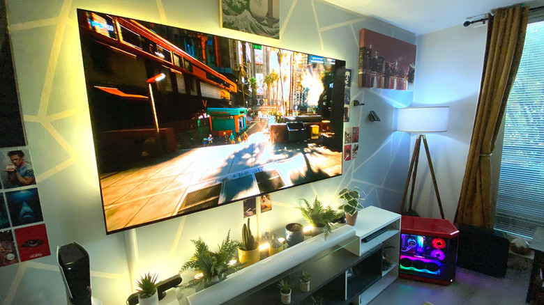 Cyberpunk 2077 showing on a TV in an entertainment center, alongside a gaming PC in a living room.