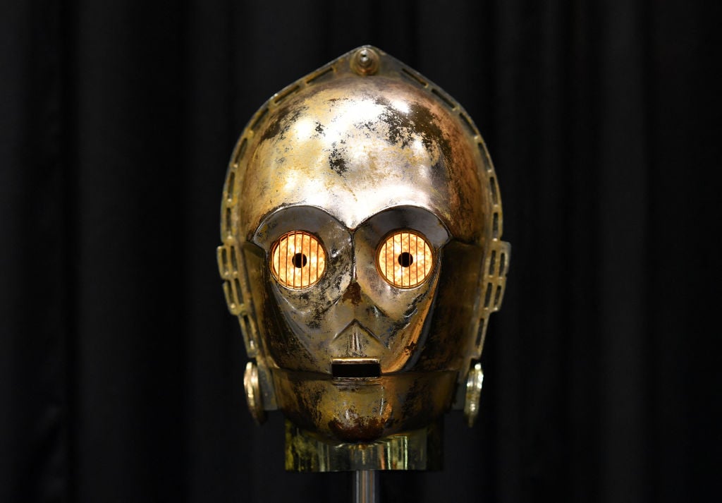 A close-up of a worn and weathered metallic robot head with glowing eyes, resembling a classic sci-fi design. The background is a solid black.