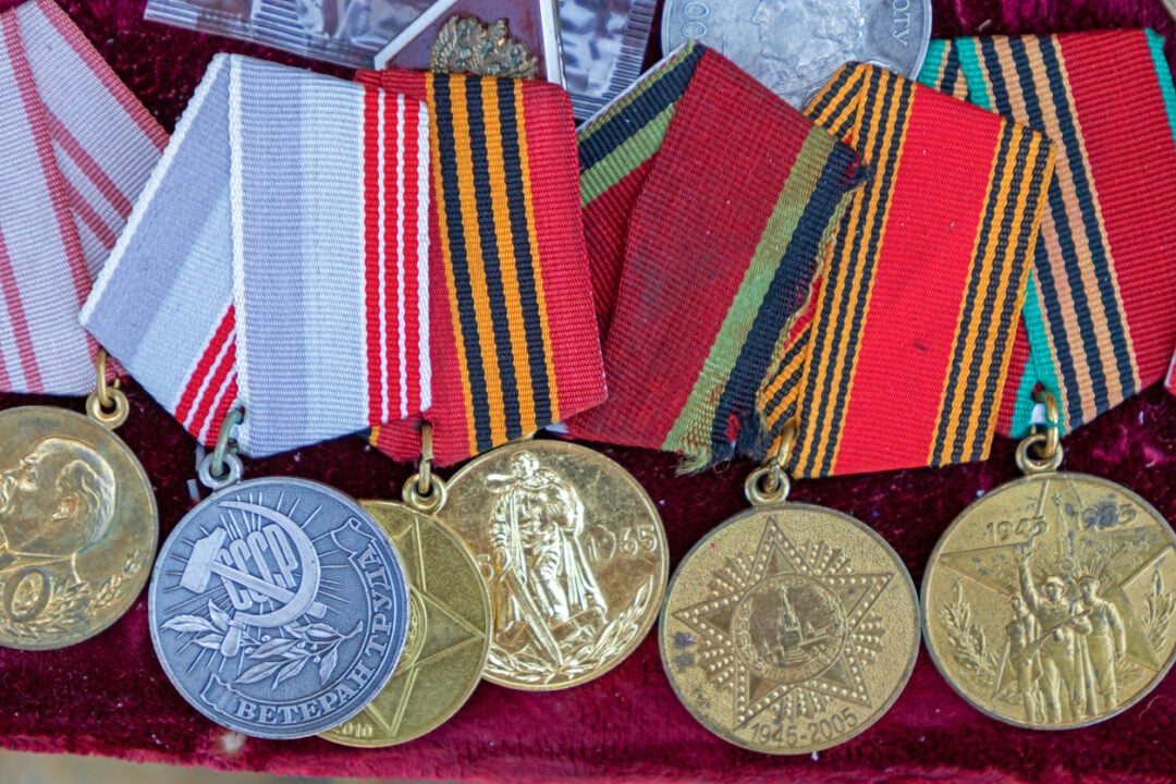 A display of six vintage medals with colorful striped ribbons, each featuring intricate embossed designs and inscriptions, arranged on a velvety background.