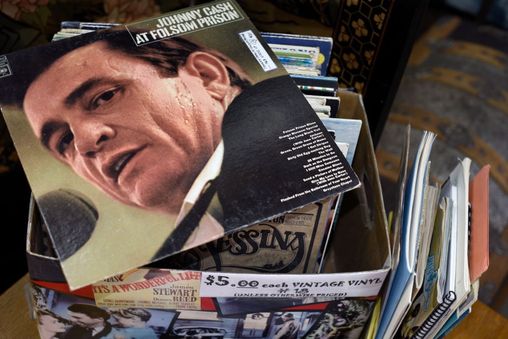 Box of vintage vinyl records with "Johnny Cash At Folsom Prison" on top. The price tag reads "$5.00 each." Various album spines and covers are visible, with a rug partially visible in the background.