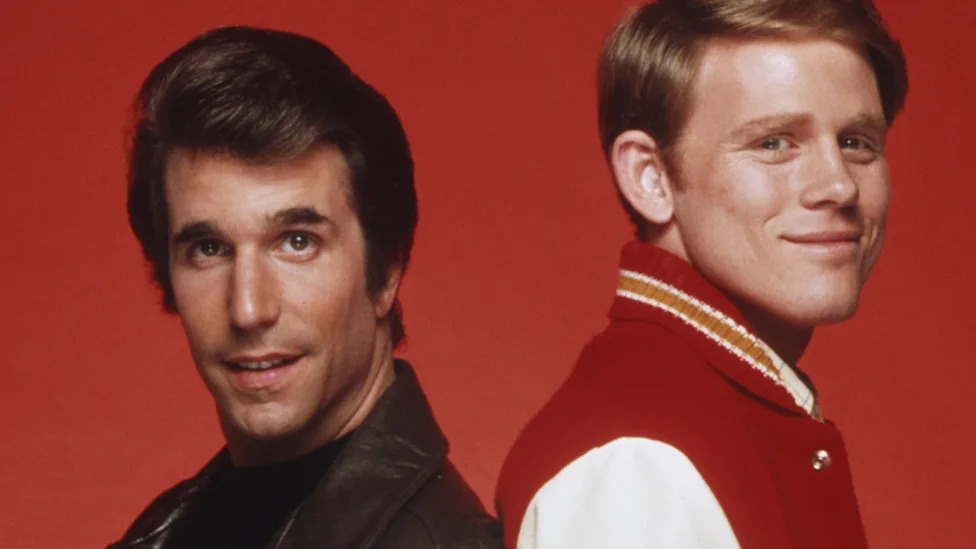 The cast of Happy Days in front of a sign reading