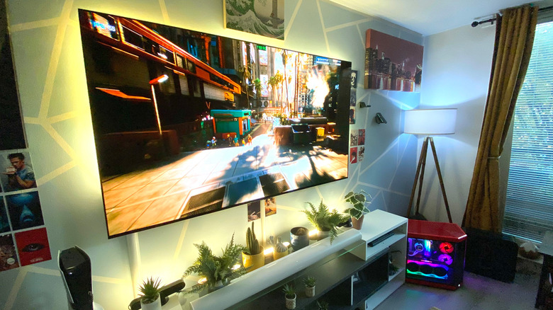 Cyberpunk 2077 on a large OLED TV in a living room, with a gaming PC in view.