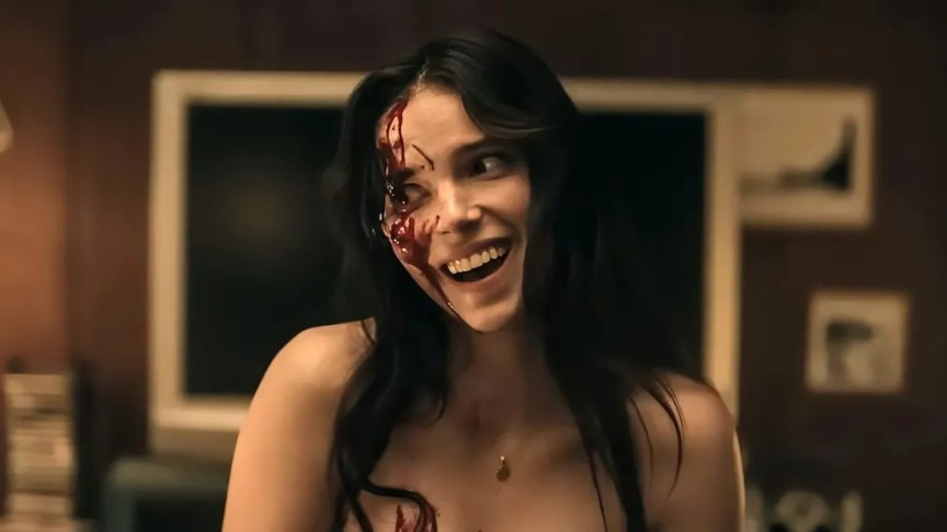 A young woman with blood on her face smiles big.