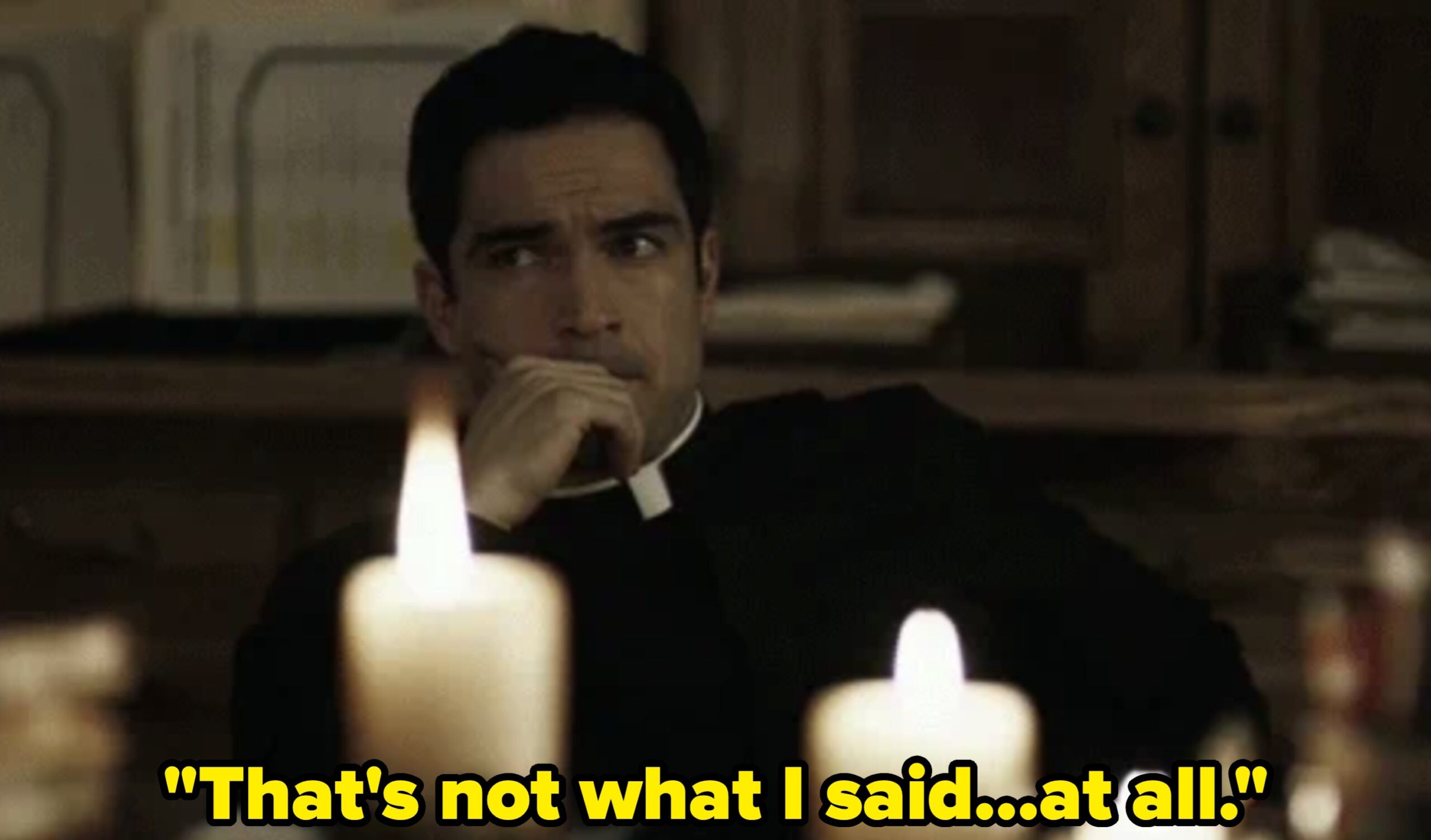 Man in religious attire sits pensively behind lit candles, suggesting contemplation or a mysterious setting