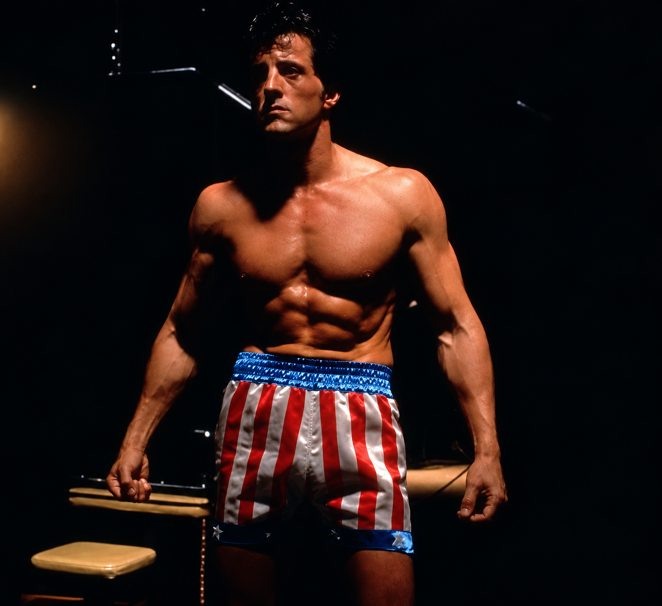 Man in boxing shorts with a USA flag design stands in a gym, exuding strength and determination