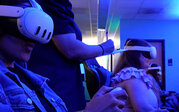 Participants wear virtual reality headsets in a blue-lit lab while a standing observer takes notes on a clipboard.