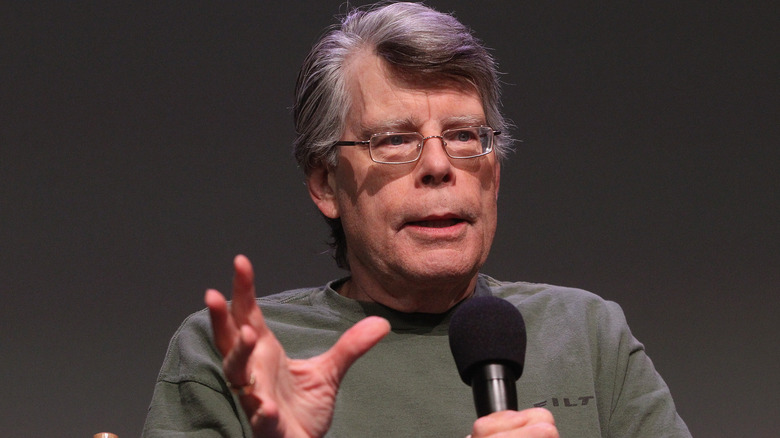 Stephen King speaks at a convention while holding a microphone